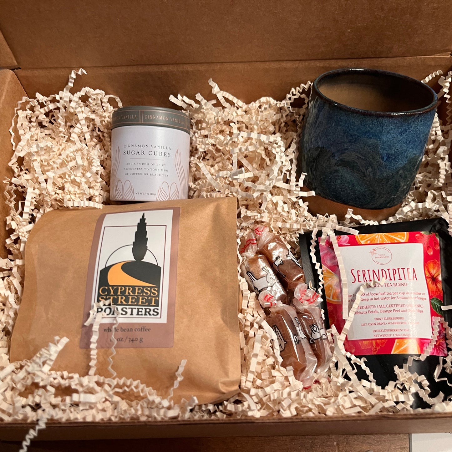This image shows a thank you box containing  coffee, tea, a pottery mug and a sweetener.