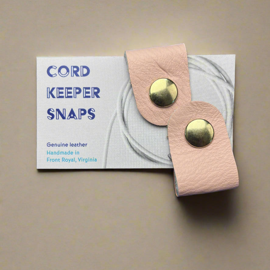 Pink leather strap with gold buttons on a Cord Keeper Snaps card against a blue background